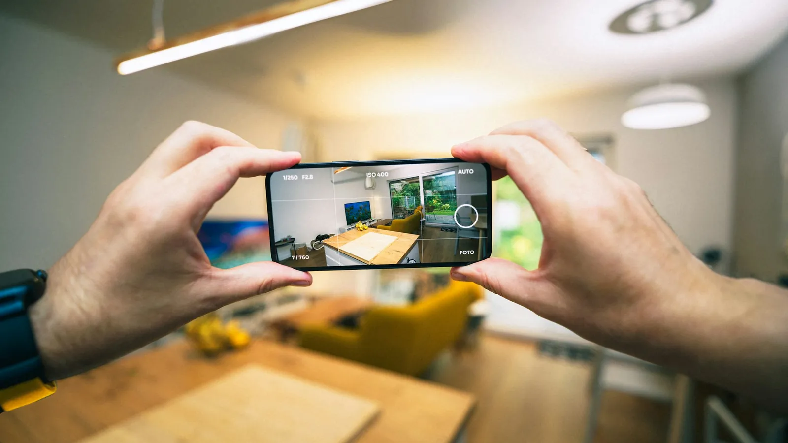 Photo immobilière au smartphone : téléphone tenu à deux mains, à l'horizontale, face à un séjour lumineux